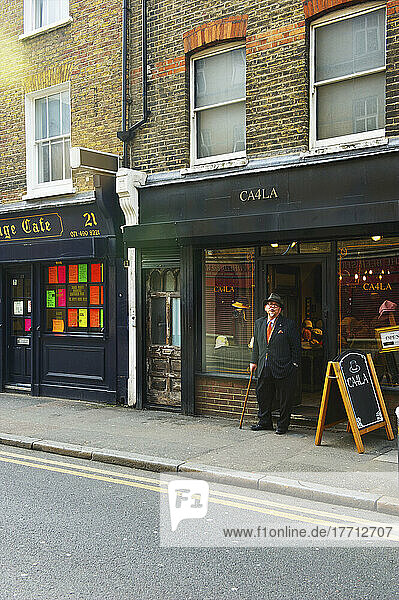 Ein älterer Mann mit Gehstock und Zylinder steht vor einem Restaurant  Shoreditch; London  England
