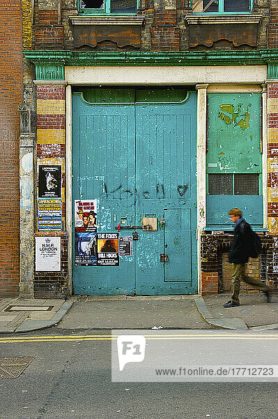Ein Fußgänger geht durch eine große blaue Tür mit Plakaten  Shoreditch; London  England