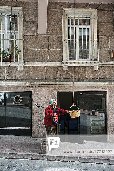 Eine Frau steht und hält einen Korb  der von einer oberen Etage eines Gebäudes hängt; Istanbul  Türkei