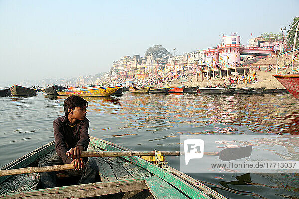 Junge rudert Boot für Touristen auf dem Ganges. Die Kultur von Varanasi ist eng mit dem Fluss Ganges und dessen religiöser Bedeutung verbunden  denn Varanasi ist die religiöse Hauptstadt Indiens und ein wichtiges Pilgerziel.