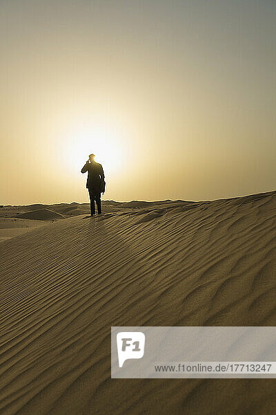 Man In Smart Suit Making Phone Call On Top Of Sand Dune At Dusk; Dubai  Vereinigte Arabische Emirate