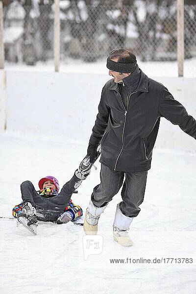 Father Dragging His Son By His Ice Skates  On An Outdoor Rink. Winnipeg  Manitoba  Canada.