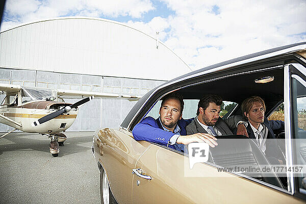 Three Businessmen Sitting In The Backseat Of A Car By An Airplane; Langley  British Columbia  Canada