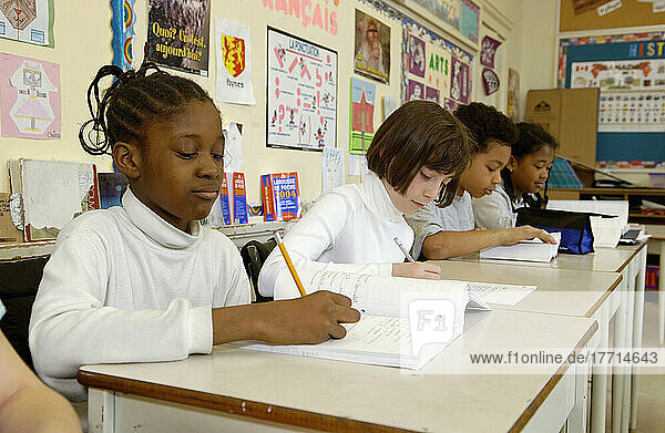 Multiethnische Gruppe von Schülern der Klasse 5 bei der Arbeit an ihren Schreibtischen in einem Klassenzimmer