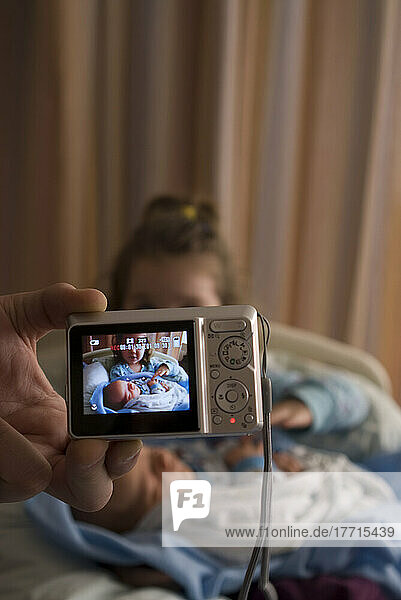 Big Sister Holding Newborn Brother In Hospital  Through Camera.