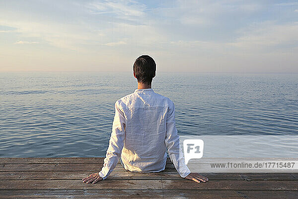 Mann sitzt auf hölzernem Dock bei Sonnenaufgang