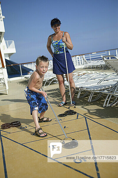 Junger Junge mit Mutter spielen Shuffle Board auf Deck des Kreuzfahrtschiffes