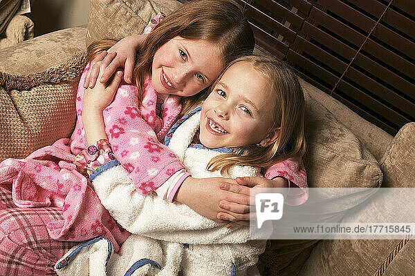 Zwei junge Mädchen umarmen auf Couch in Pyjamas