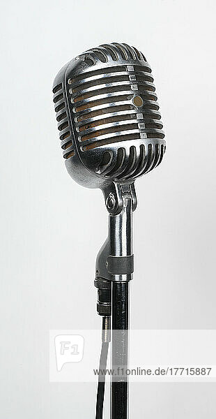 Nahaufnahme eines alten  verchromten Studiomikrofons auf einem Ständer vor einem weißen Hintergrund; Studioaufnahme