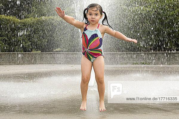 Junges asiatisch-weißes Mädchen springt und spielt in einem Wassersprinkler; Ontario Kanada