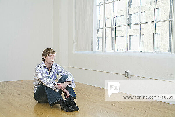 Mann  der auf dem Boden eines leeren Raums sitzt
