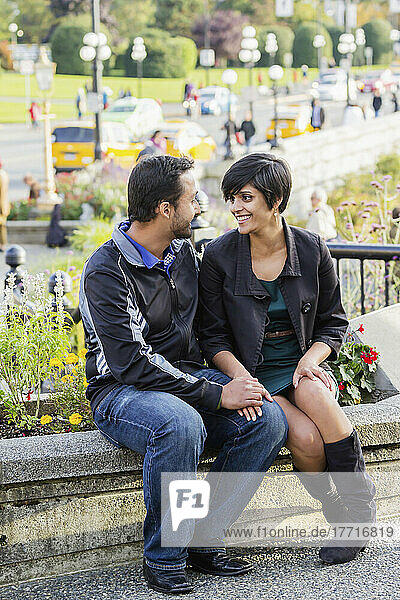 A Young Indian Ethnicity Couple Sit Together Smiling Romantically; Victoria  Vancouver Island  British Columbia