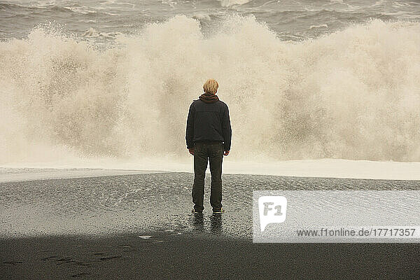 Mann  der vor großen Wellen an einem schwarzen Sandstrand in der Nähe von Vik  Island  steht