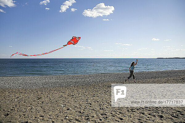 Frau läuft und lässt einen roten Drachen am Strand des Ontariosees steigen; Ontario Kanada