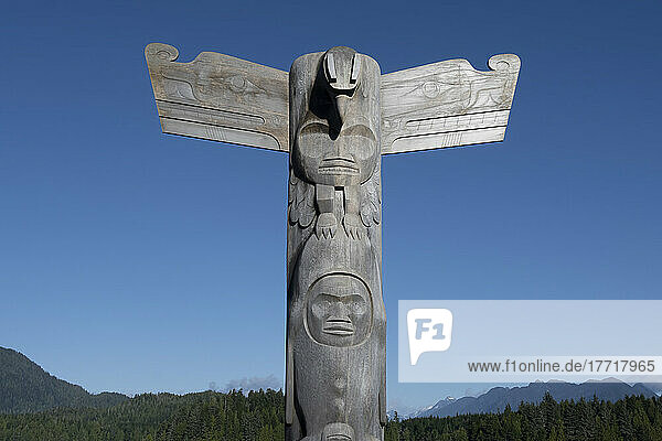 Totempfahl  eine Art Kunst der Nordwestküste  mit blauem Himmel  gemäßigtem Regenwald und Bergkette im Hintergrund; Tofino  British Columbia  Kanada