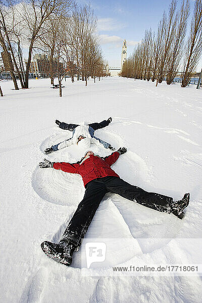 Mädchen machen Schneeengel mit Uhrenturm im Hintergrund