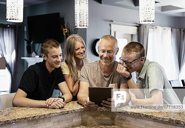 Eltern und zwei Söhne sitzen zu Hause an der Kücheninsel  verwenden ein Tablet und sehen sich gemeinsam Inhalte an; Edmonton  Alberta  Kanada