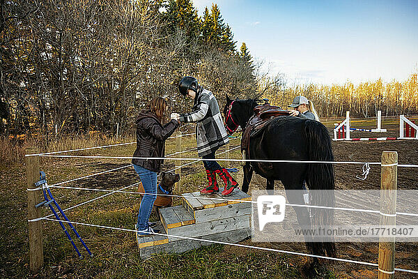 Ein junges Mädchen mit Cerebralparese steigt während einer Hippotherapie-Sitzung mit Hilfe ihrer Mutter und ihres Trainers von ihrem Pferd ab; Westlock  Alberta  Kanada
