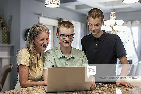Junger Mann benutzt zu Hause einen Laptop mit Unterstützung seiner Mutter und seines Bruders; Edmonton  Alberta  Kanada
