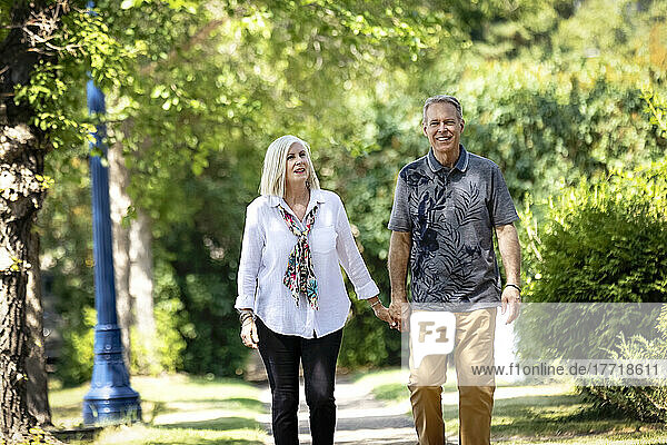 Mature couple holding hands while walking outdoors on a park trail; Edmonton  Alberta  Canada