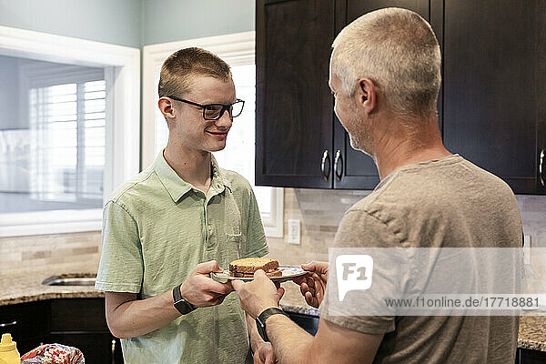 Young man serving his dad a sandwich in the kitchen at home; Edmonton  Alberta  Canada
