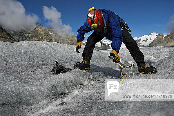 An expedition leader fixing an ice screw to anchor a rope before descending down into a moulin.