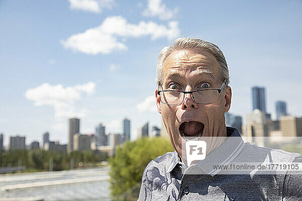 Ein älterer Mann steht im Freien und blickt mit einem überraschten Gesichtsausdruck über seine Brille hinweg in die Kamera; Edmonton  Alberta  Kanada