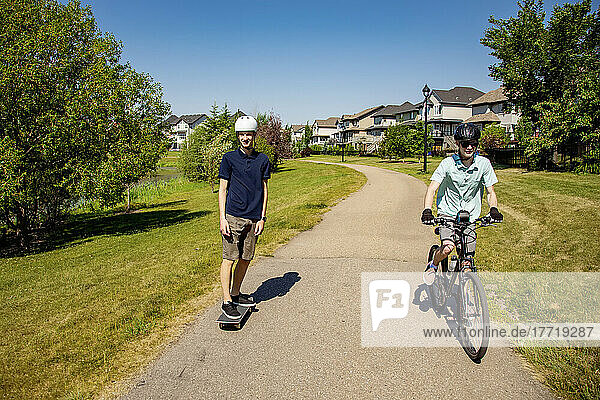 Brüder  die gemeinsam Zeit in der Nachbarschaft verbringen  einer auf einem Fahrrad und einer auf einem Skateboard; Edmonton  Alberta  Kanada