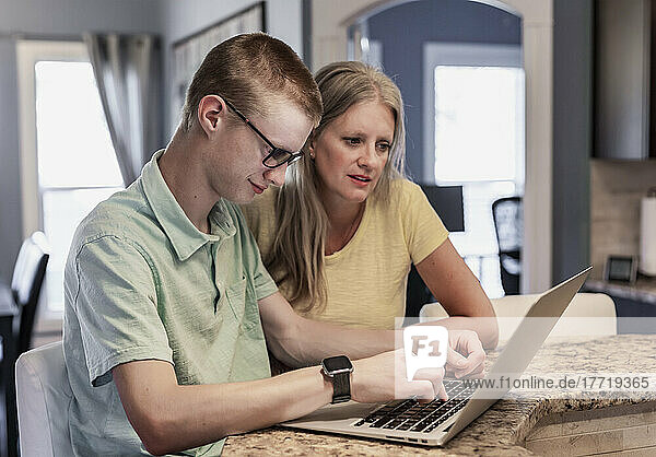 Junger Mann benutzt zu Hause einen Laptop mit Unterstützung seiner Mutter; Edmonton  Alberta  Kanada
