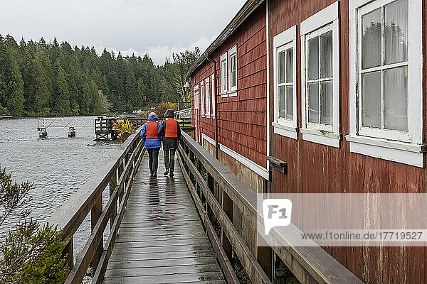 Two people wearing lifejackets walk together and enjoy the harbour in the village of Bamfield  Vancouver Island; British Columbia  Canada