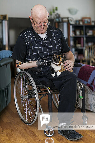 Man with double limb amputations sitting in his house with his pet in his lap; St. Albert  Alberta  Canada