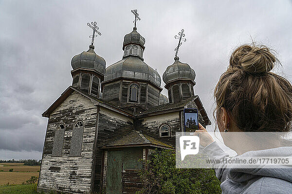 Frau  die mit ihrem Smartphone Fotos von einer alten Kirche im ländlichen Saskatchewan macht; Maryville  Saskatchewan  Kanada