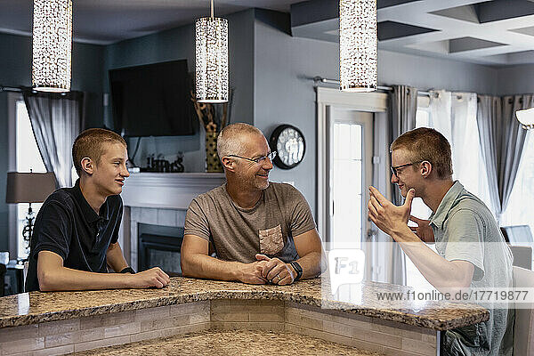 Vater und zwei Söhne sitzen zu Hause an der Kücheninsel und reden miteinander; Edmonton  Alberta  Kanada