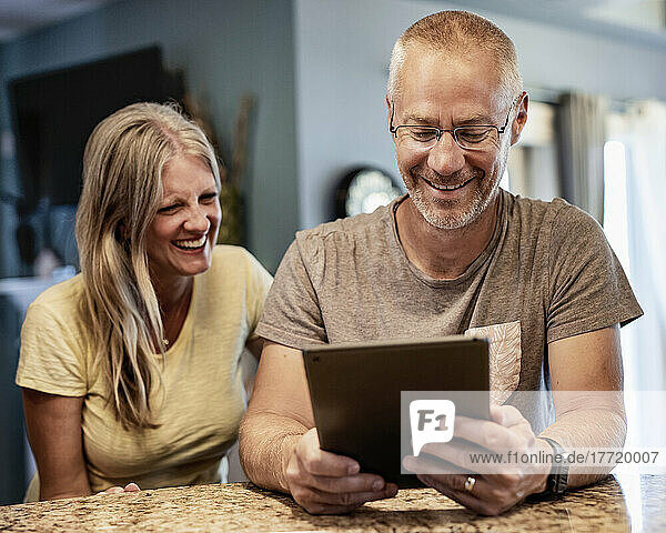 Mature couple sitting a home laughing together at content on a tablet; Edmonton  Alberta  Canada