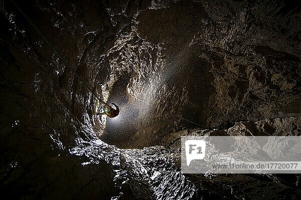 Der Expeditionsleiter nimmt eine Verankerung in Angriff (vorbei an einer Kreuzung von zwei an der Wand befestigten Seilen) und setzt seinen Weg in die Tiefe der Veryovkina-Höhle fort. Dieses Foto markiert die Stelle in der Höhle  an der man zum ersten Mal auf Wasser trifft. Ein riesiger Zulauf  der von einem direkten Weg an die Oberfläche gespeist wird  stürzt in die Höhle. Glücklicherweise war an dem Tag  an dem wir die Höhle erkundeten  das Wetter an der Oberfläche freundlich (im Gegensatz zum letzten Jahr)  und es stürzte nicht allzu viel Wasser auf uns herab; Gagra  Kaukasusgebirge  Abchasien