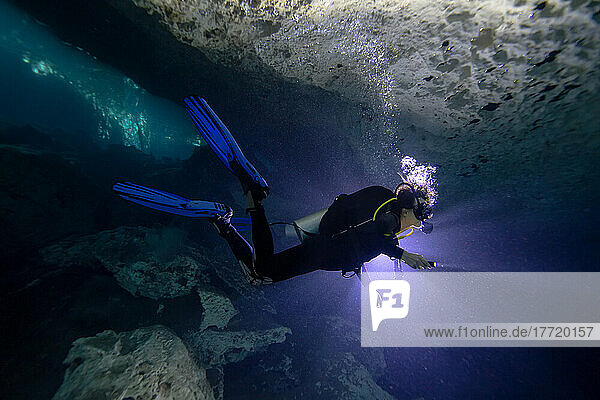 Scuba diver exploring an underwater cave with a light; Tulum  Quintana Roo  Mexico