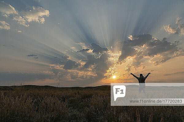Korpuskulare Strahlen bei Sonnenaufgang über der Prärie von Saskatchewan. Frau steht und freut sich über die Schönheit eines neuen Tages; Saskatchewan  Kanada