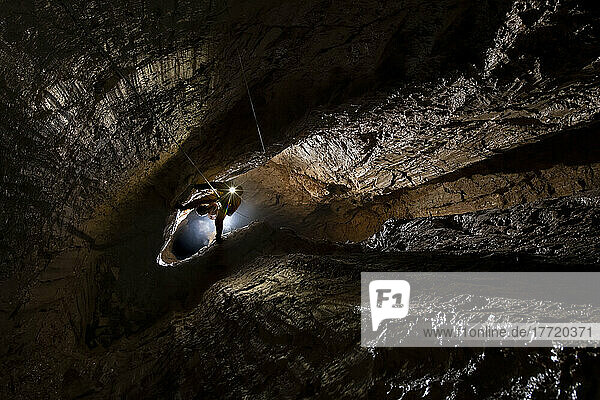 Der Expeditionsleiter hängt an einem Seil  das seine Beine über den engen Spalt zwischen zwei Wänden in der Veryovkina-Höhle spannt. Der größte Schacht der Eingangsserie ist etwa 50 m tief. Dieses Foto zeigt den Blick nach unten über die obere Hälfte des Schachts; Gagra  Kaukasus  Abchasien