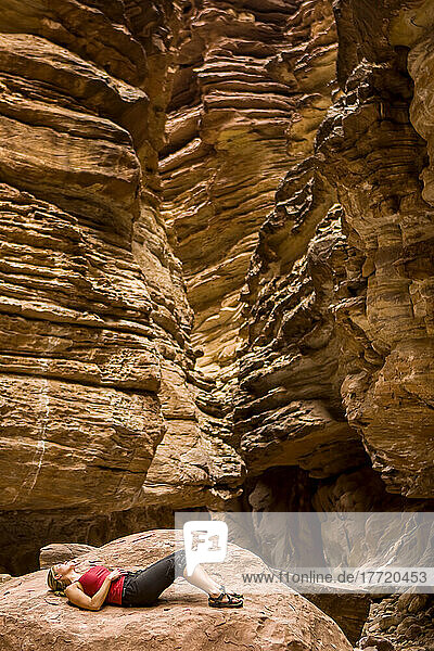 Ein Wanderer entspannt sich auf einem großen Felsen im Blacktail Canyon am Colorado River bei Meile 120 im Rahmen des Arizona Highways Photography Workshop; Grand Canyon National Park  Arizona  Vereinigte Staaten von Amerika