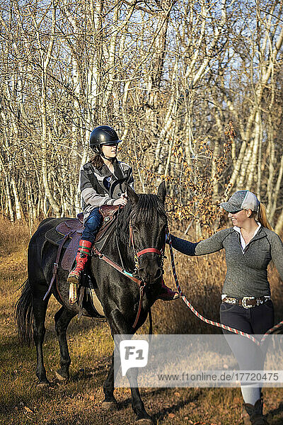 A young girl with Cerebral Palsy and her trainer working with a horse on a trail ride during a Hippotherapy session; Westlock  Alberta  Canada