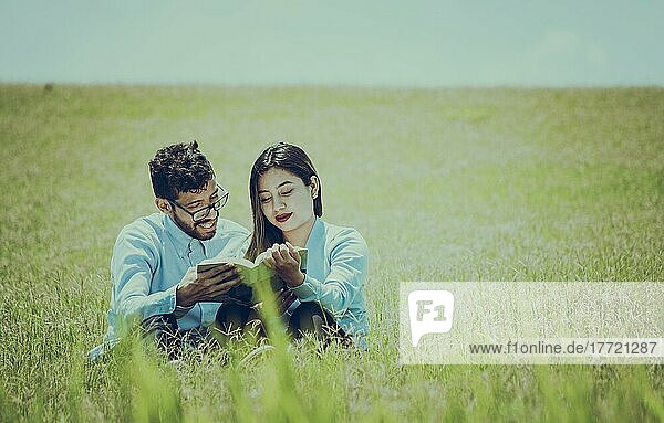 Ein Paar  das im Gras sitzt und ein Buch liest  Zwei Menschen  die im Gras sitzen und ein Buch lesen  Konzept von Menschen  die draußen lesen