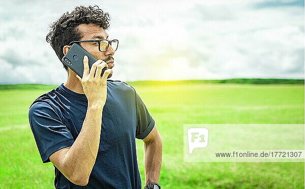 Person with his cell phone in the field calling on the phone  Man calling on the phone in the field  man on a road talking on the phone  young person talking on the phone in a field