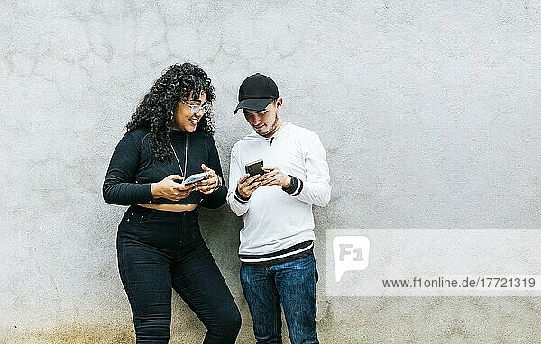 Zwei Teenager  die ihre Handys überprüfen und lächeln  die zusammen ihre Handys überprüfen  Ein Junge und ein Mädchen  die sich an eine Wand lehnen und ihre Handys überprüfen  Zwei lächelnde Freunde  die ihre Handys überprüfen