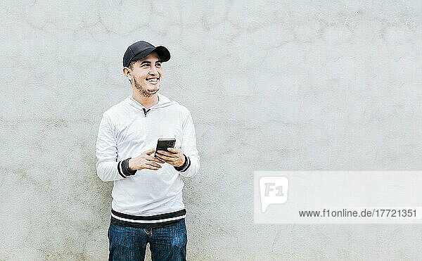 Hübscher Kerl glücklich mit seinem Handy  junger lateinamerikanischer Mann glücklich mit seinem Handy gegen eine Wand gelehnt. Ein junger lateinamerikanischer Mann lacht mit seinem Handy  das an einer Wand lehnt