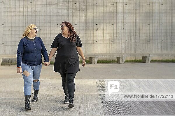 Latin lesbischen Paar Blick auf einander mit Zuneigung zu Fuß Hand in Hand auf der Straße