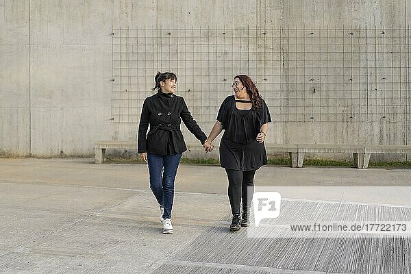 Lateinisches lesbisches Paar  das sich liebevoll anschaut und Hand in Hand auf der Straße geht. Raum kopieren