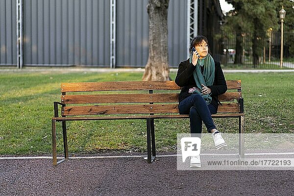 Lateinamerikanische Frau  die auf einer Bank im Park sitzt und mit einem Handy telefoniert