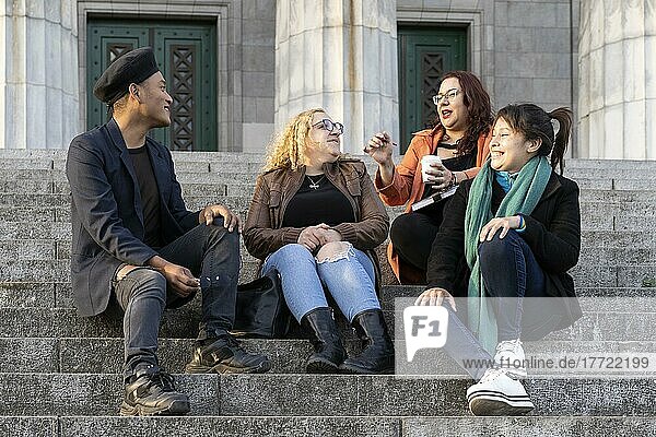 Eine multiethnische Gruppe von Freunden sitzt auf einer Treppe und unterhält sich und lacht