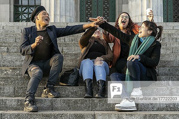 Eine multiethnische Gruppe von Freunden sitzt auf einer Treppe und unterhält sich und lacht