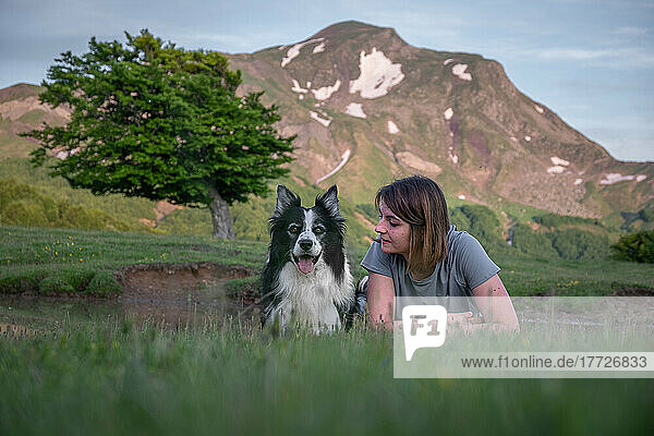 A girl and her border collie dog lying in the grass with a tree and mountain in the background  Emilia Romagna  Italy  Europe